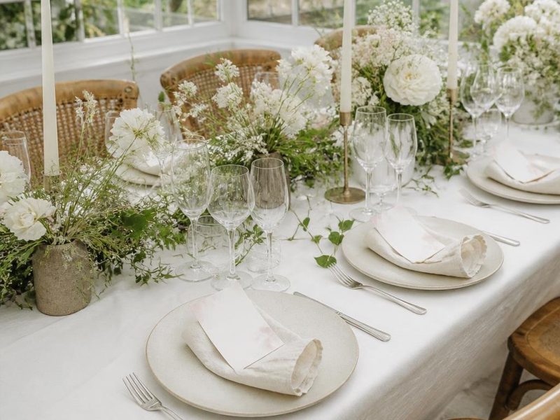 Table de mariage lumineuse avec cartes menu marque-place, serviettes en lin et fleurs blanches.